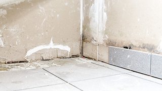 Verfärbte Wand mit beschädigtem Bodenbereich in der Ecke